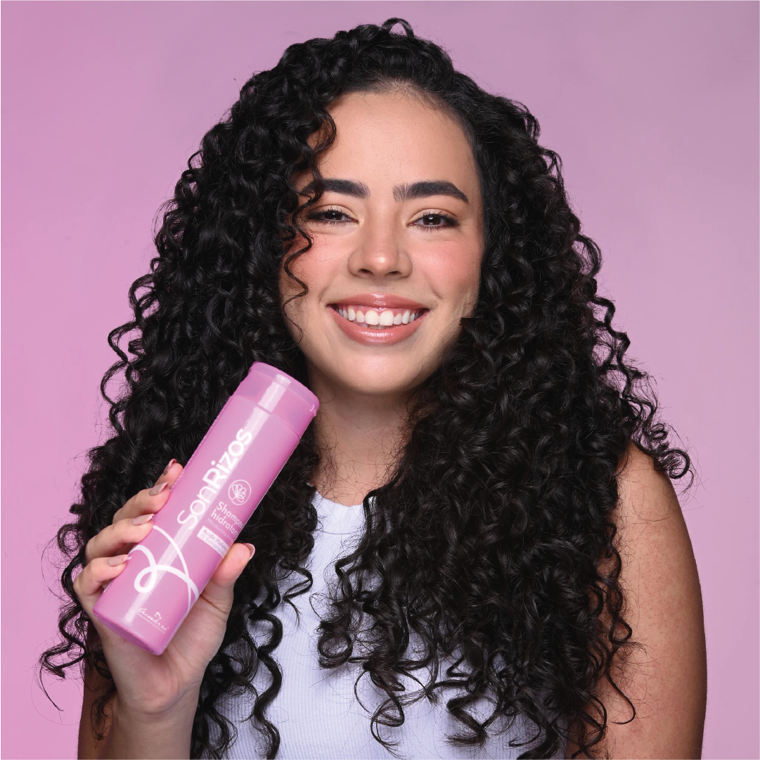 Mujer de cabello rizado negro sonriendo con un producto SonRizos en la mano