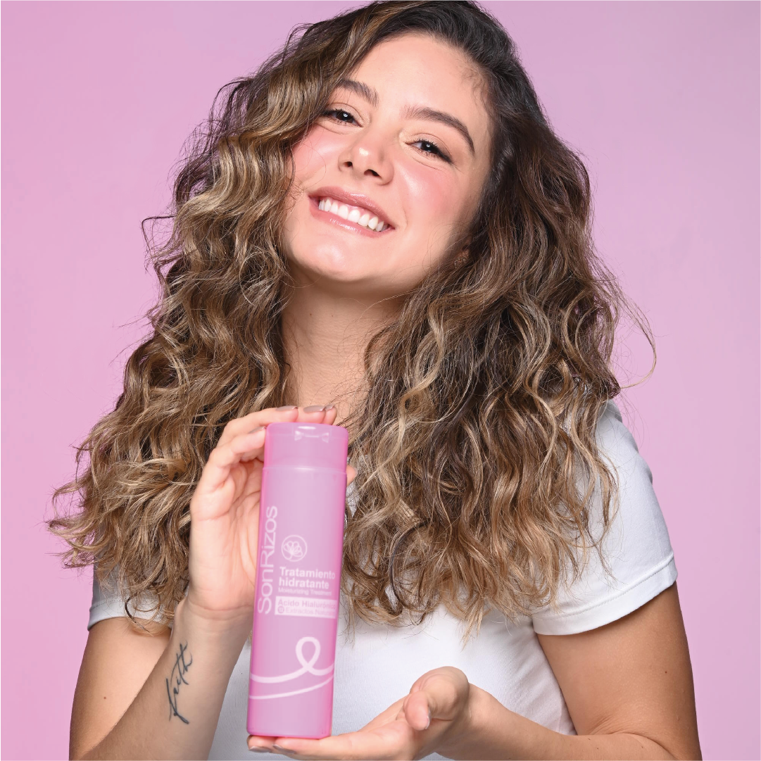 Mujer de cabello ondulado castaño sonriendo con un producto SonRizos