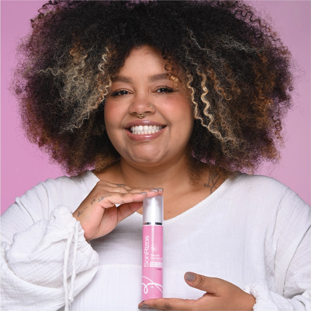 Mujer de cabello afro con mechas claras sosteniendo el sérum capilar SonRizos